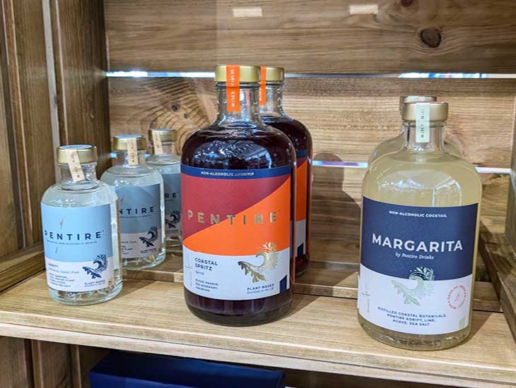 Bottles of non-alcoholic cocktails displayed on a wooden shelf. The prominent bottle in the center is labeled 